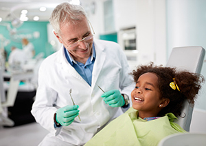 Dentist with dental cleaning tools and child patient sitting in dental exam chair.